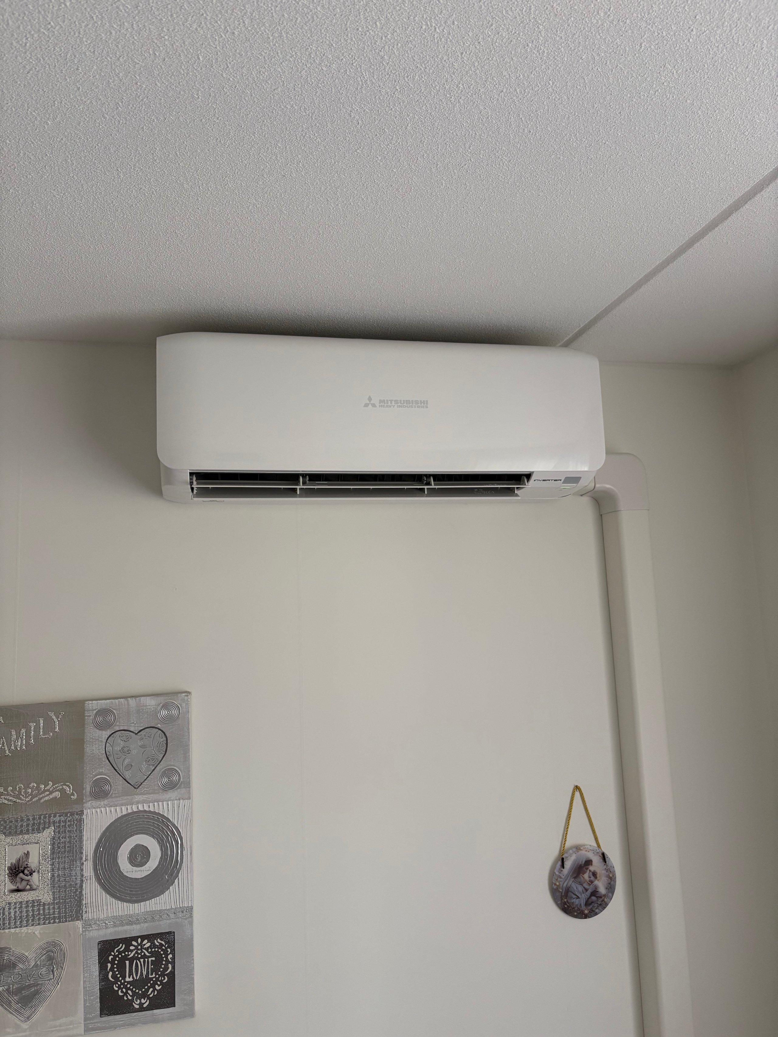 White ductless air conditioning unit mounted on a bedroom wall above framed wall decor