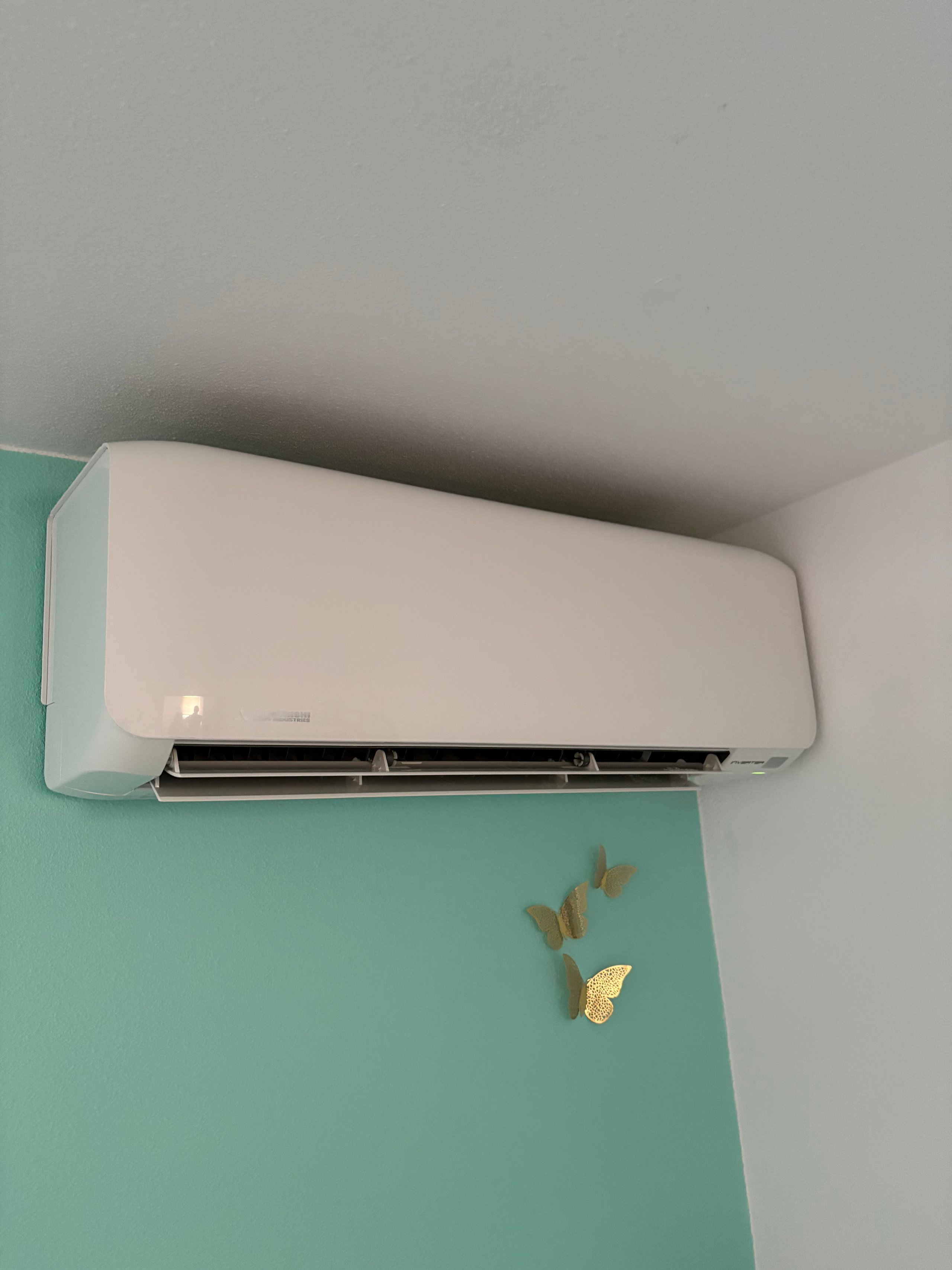White and mint green split-type air conditioning unit mounted on turquoise wall with decorative gold leaf elements below