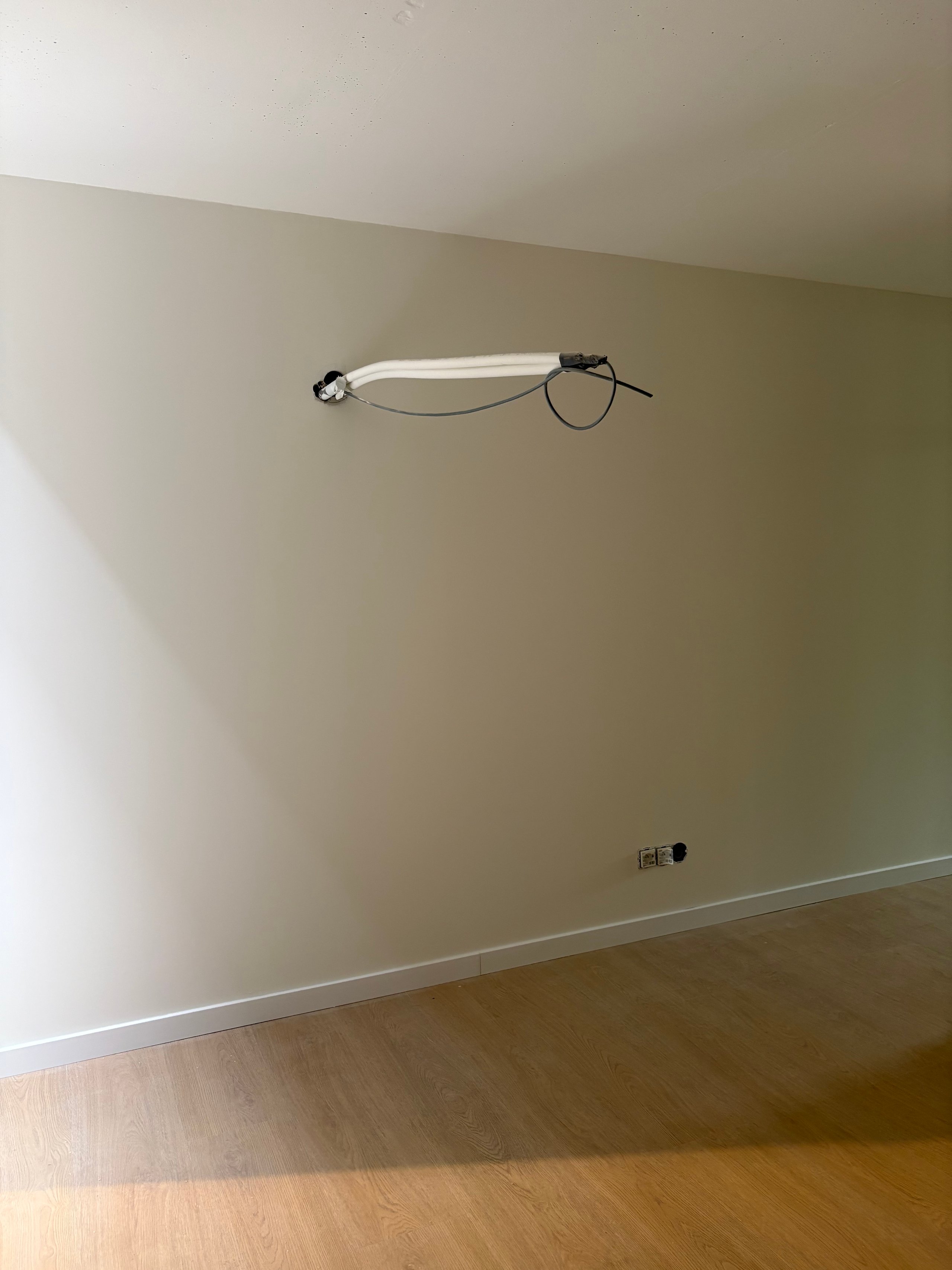 A horizontal fluorescent ceiling light fixture mounted on a pale green wall above wooden flooring with electrical outlets visible below