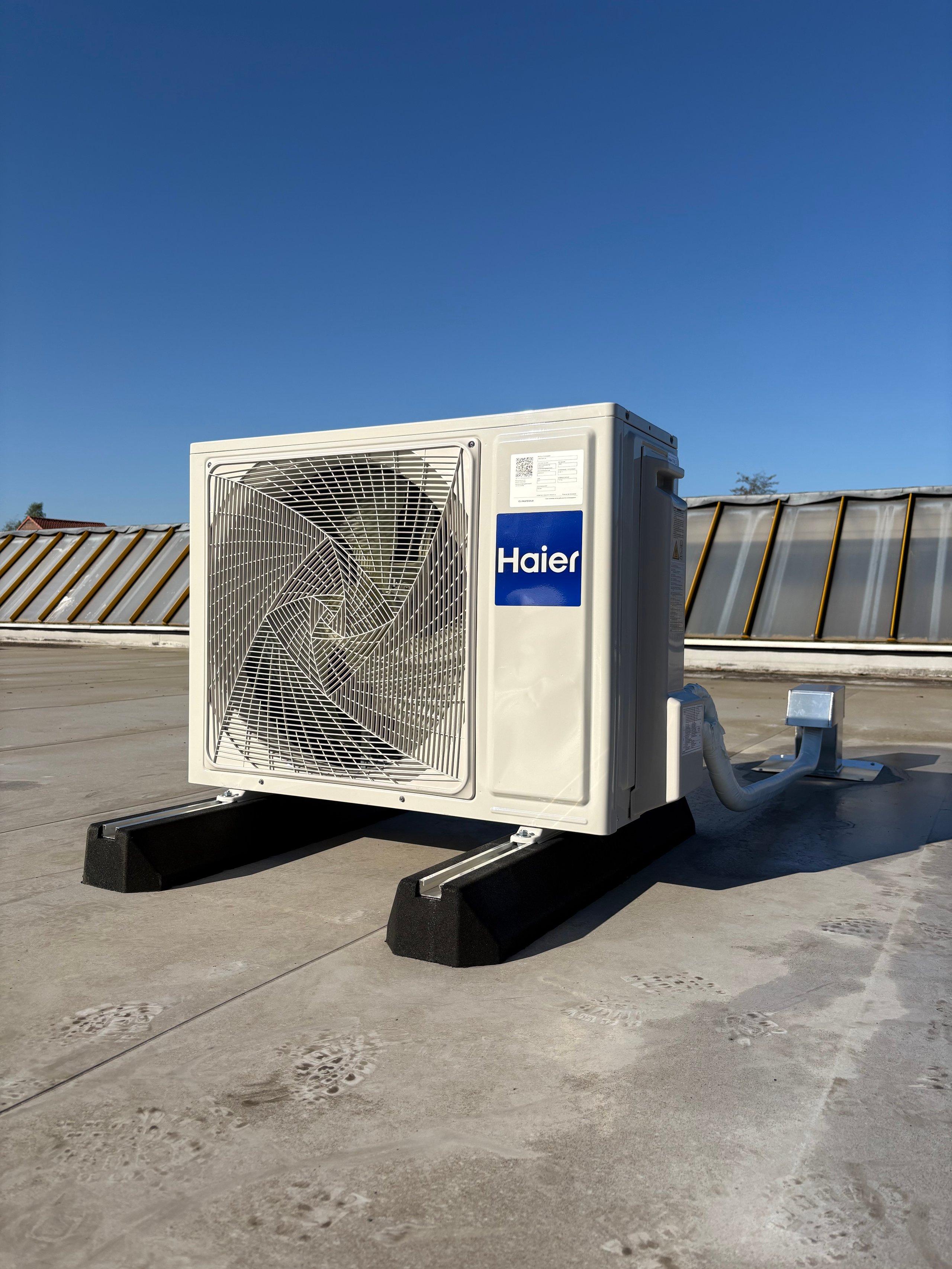 Haier HVAC outdoor unit installed on a rooftop with metal vents and clear blue sky in the background