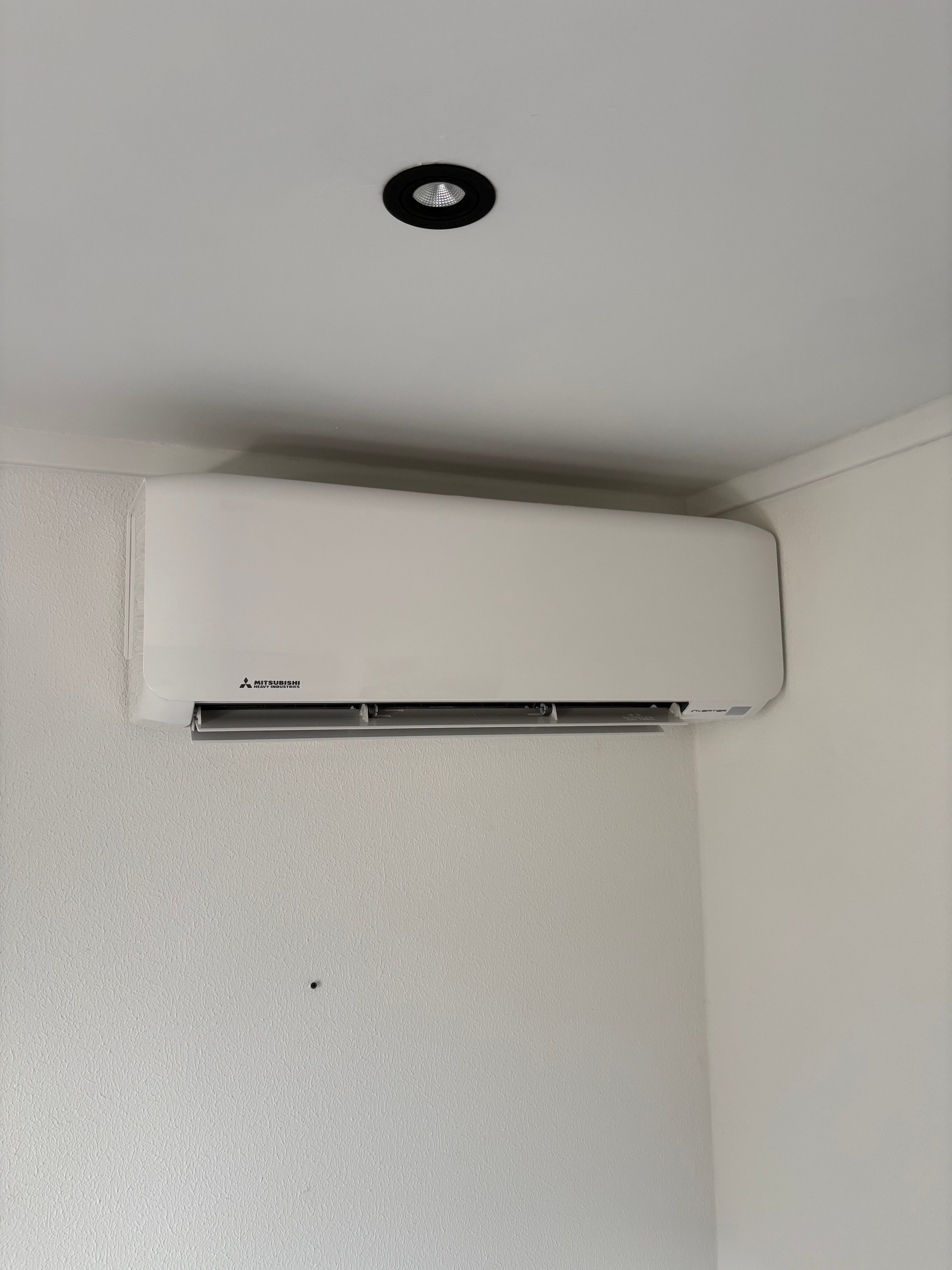 White Mitsubishi ductless air conditioning unit mounted on a white wall with a black ceiling vent above it