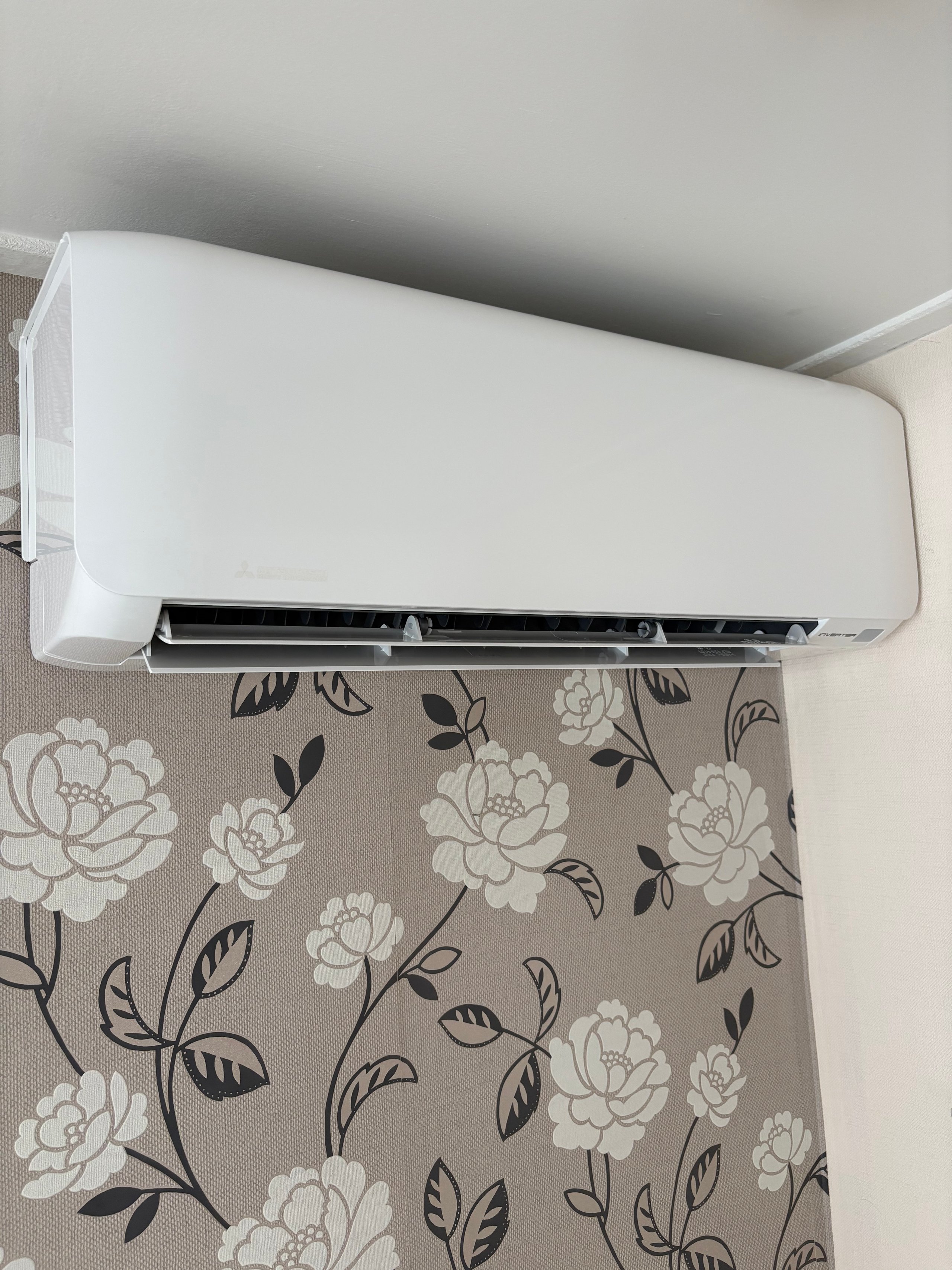 White air conditioning unit mounted on beige floral patterned wallpaper on an interior wall