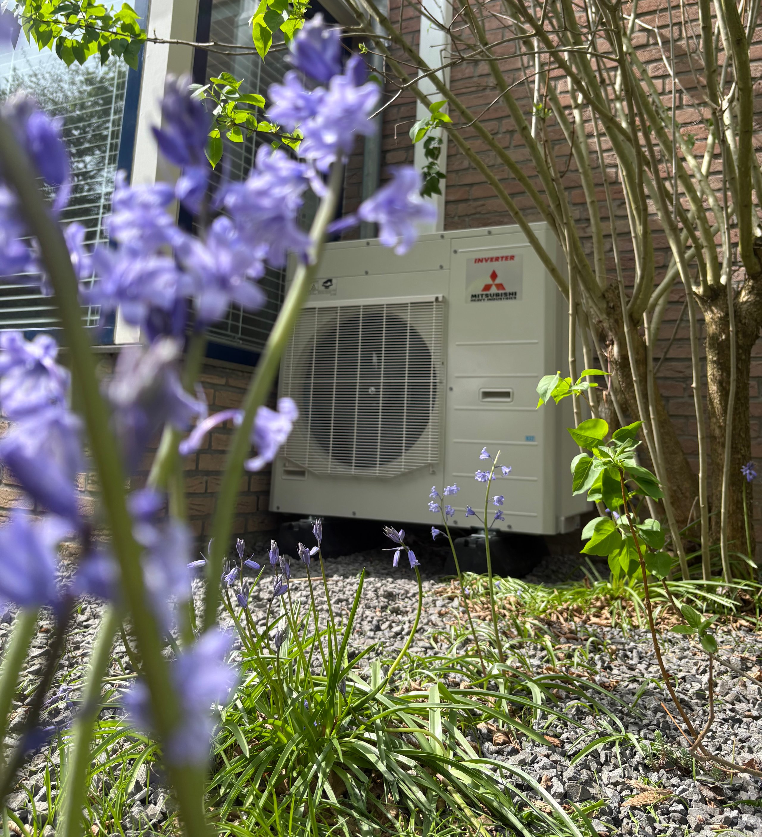 Mitsubishi heat pump unit in garden setting with purple flowering plants