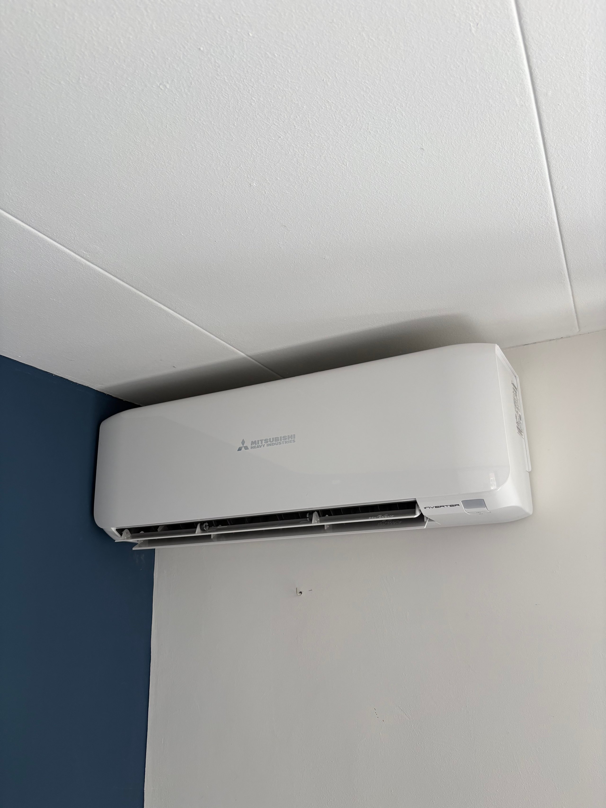 White Mitsubishi split air conditioning unit mounted on wall below white ceiling