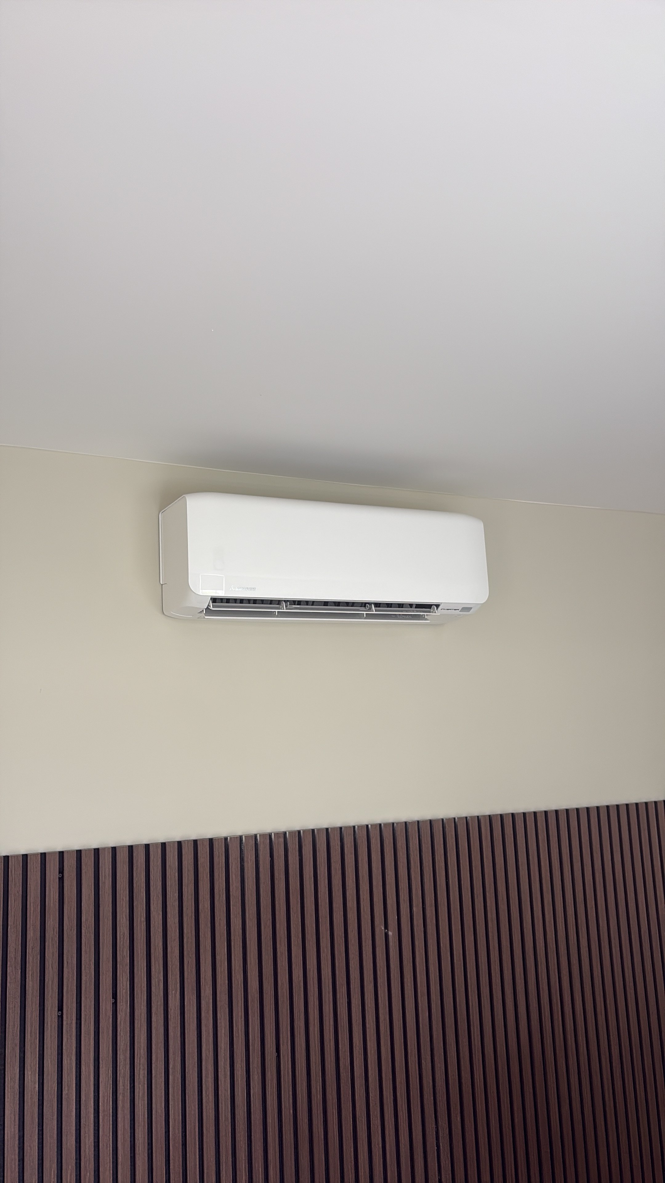 White split air conditioning unit mounted on beige wall above dark ribbed wall paneling